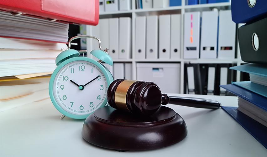 A gavel and alarm clock on a desk with folders behind, signifying legal action against U.S. citizenship and immigration service at federal courts.