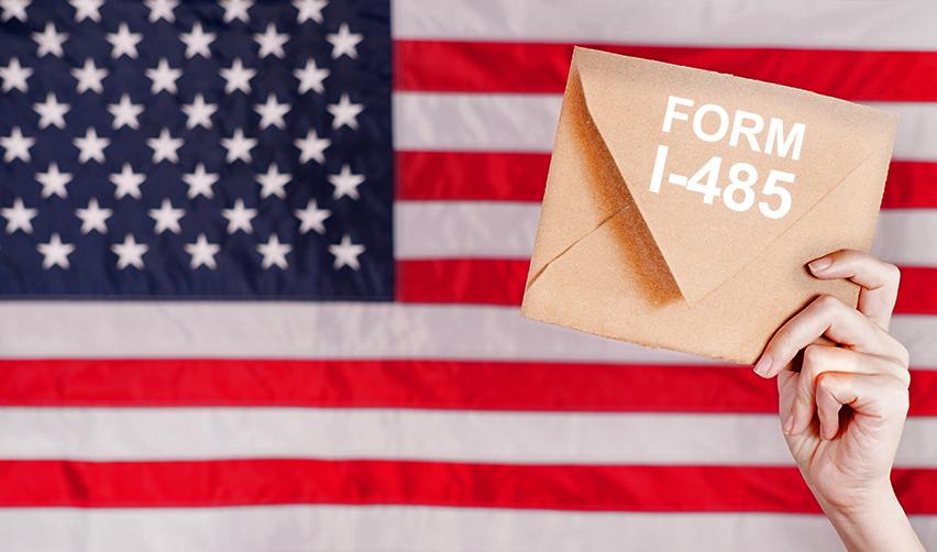 An envelope that reads Form I-485 held up in front of an American flag.