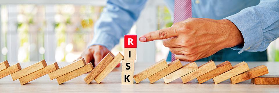 A person pointing at blocks of wood with the word risk spelled out.