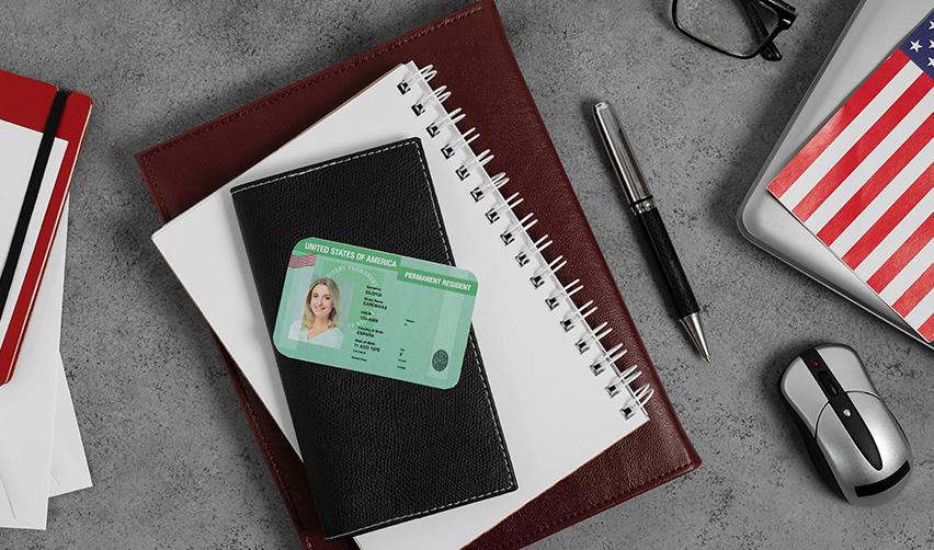 Notebooks, documents and a pen on a desk, with a United States Permanent Resident Card (Green Card) on top.