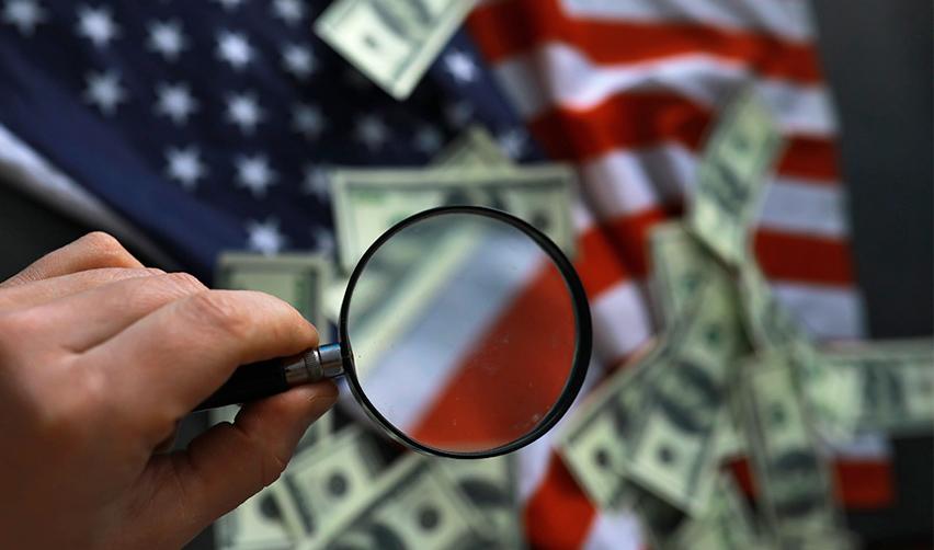 A magnifying glass over some dollar bills on an American flag.