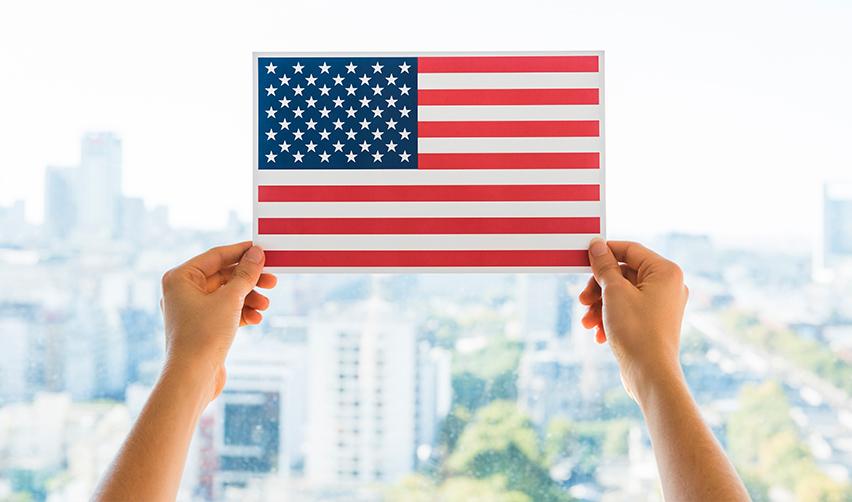 Hands holding a U.S. flag in front of a window with a city view in the background