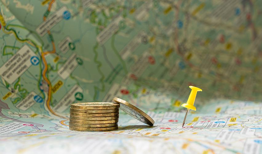 A close up of a map with a pin marking the location of a rural area and a stack of coins on it.