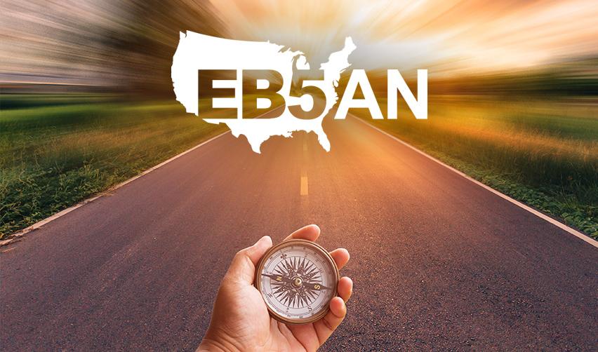 A hand holding a compass on a road with the EB5AN logo above it.