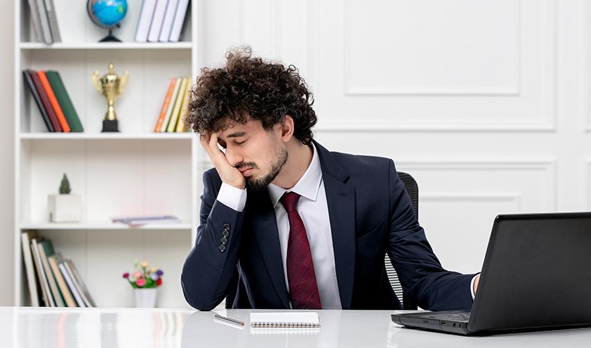 A distressed H1B worker sitting at a desk with his hand on his face.