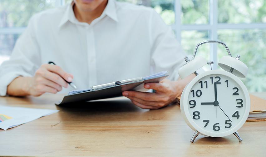 An EB5 investor sitting at a desk with an adjustment of status application, with a white clock on the desk symbolizing i-485 processing time.