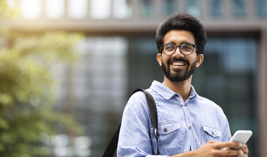 An international student visa holder holding his phone in his hands and smiling.