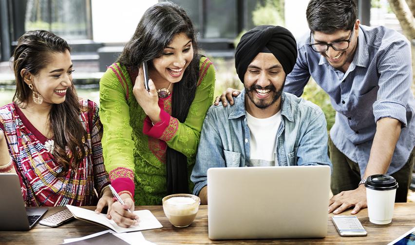 A group of Indian green card holders looking at a computer screen and smiling.