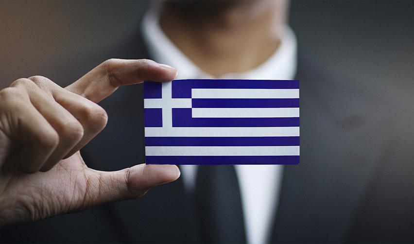 A close-up of a hand holding a small Greek flag, symbolizing the Greece golden visa.