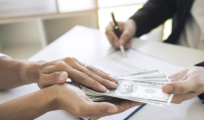 Hands of a foreign investor receiving their eb5 investment return with an immigration attorney or regional center representative signing some documents in the background.