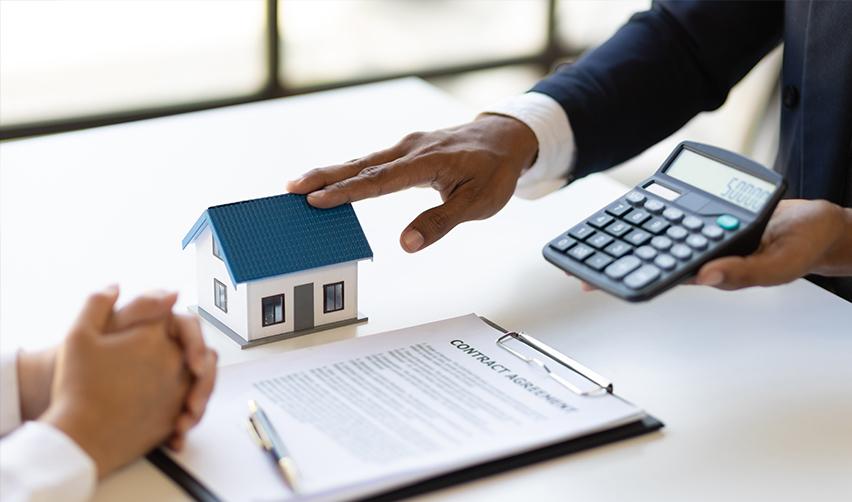 A person holding a calculator over a small house and a contract, referring to home equity line of credit or HELOC for EB5 investments.