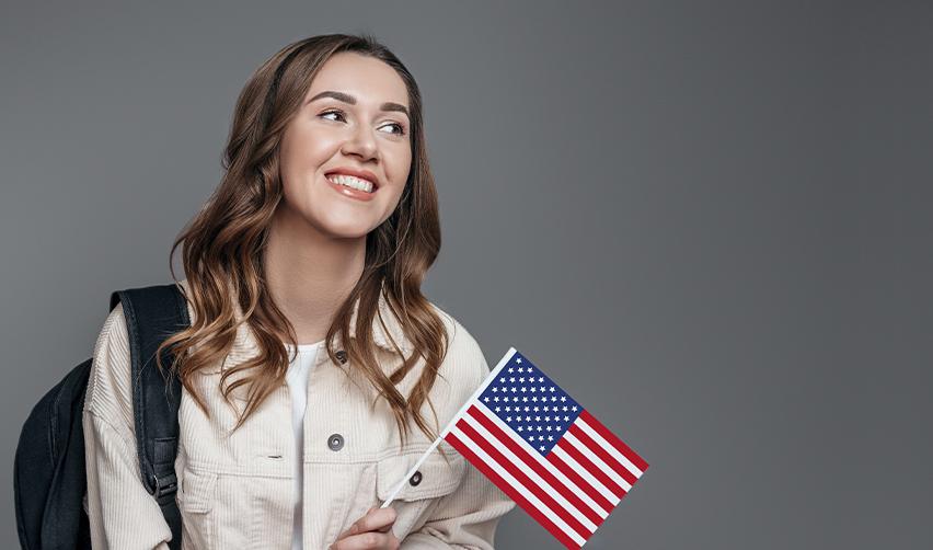 An international student smiling with a U.S. flag in her hand.