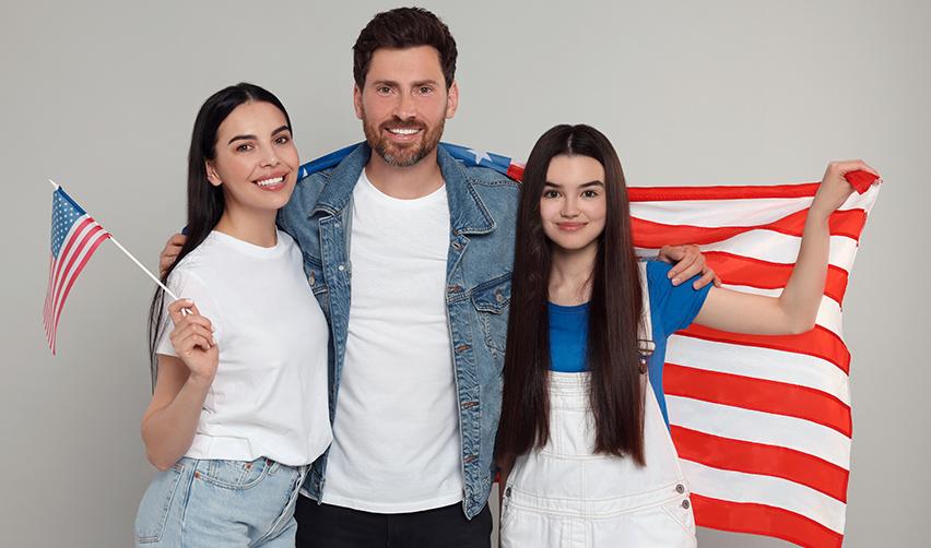 A family of Eb5 green card holders smiling at the camera with American flags in their hands.