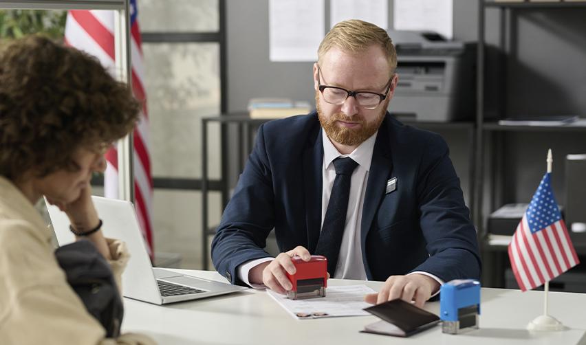 A visa officer at the national visa center stamping the visa application documents of a green card applicant.