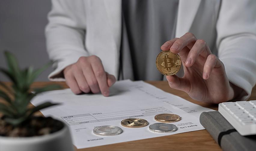 An EB5 industry professional working on some investment documents with a bitcoin in their hand.