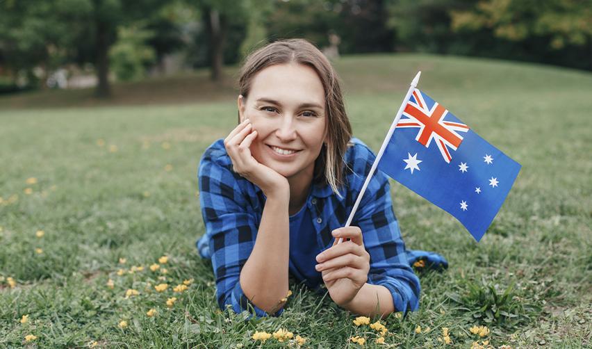 An EB5 investor holding the Australian flag and smiling at the camera, symbolizing a US green card for Australian citizens.