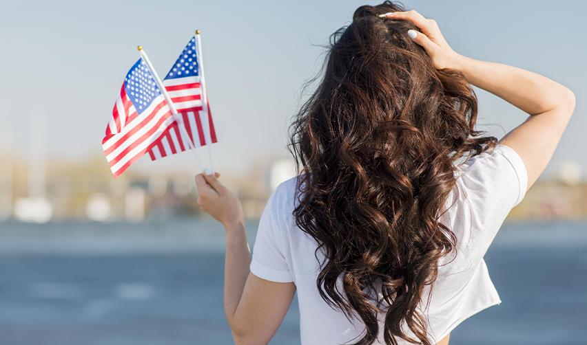 Young woman holding American flags, symbolizing the dream of achieving US permanent residency through the EB5 program.