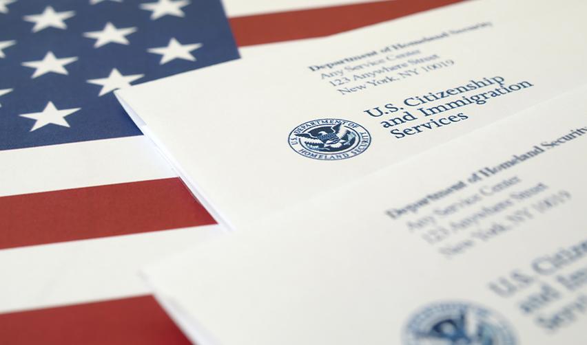 Official USCIS envelopes on an American flag background, emphasizing key distinctions between NOIDs and RFEs for EB5 applicants.