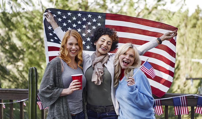 Diverse group of women celebrating with an American flag, reflecting the freedom and unity that comes with US citizenship.