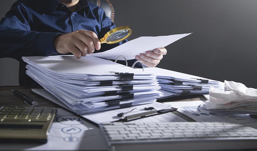 A person inspecting documents with a magnifying glass, symbolizing careful review of financial records and documents to ensure compliance with EB5 source-of-funds requirements.