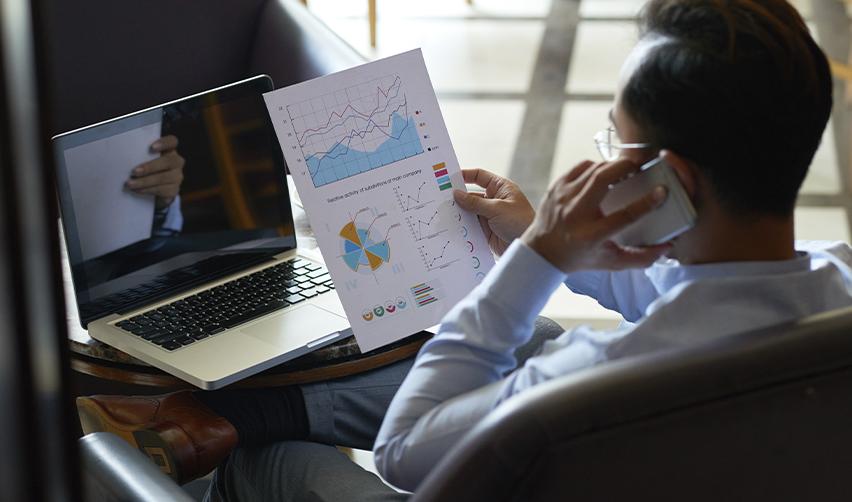 Investor analyzing financial charts and reports while discussing EB5 trends on the phone, demonstrating data-driven decision-making in EB5 investments.