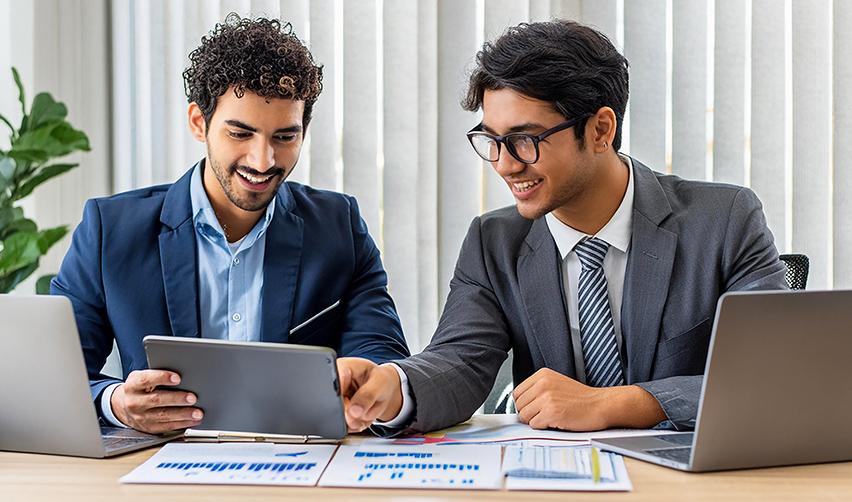 Two alien entrepreneurs discussing EB5 visa benefits for H1B workers in 2025, analyzing investment opportunities on a tablet.