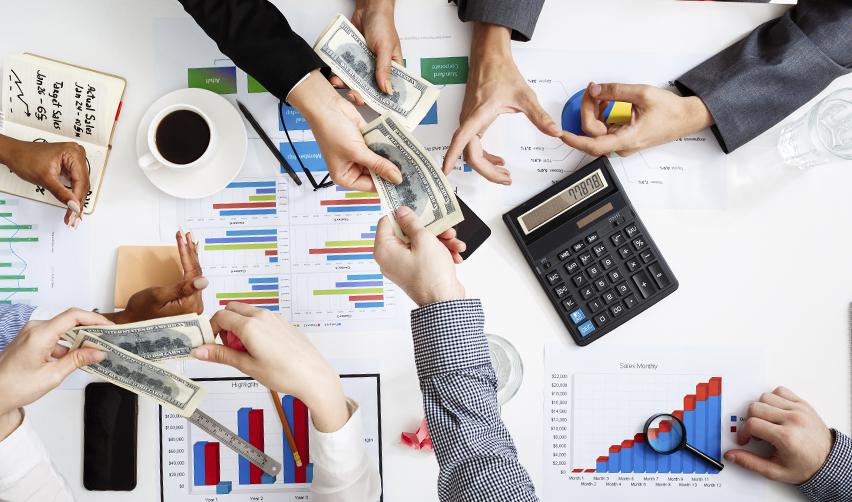 Hands exchanging money over financial charts and graphs, symbolizing EB5 investments and the financial aspects of US green card opportunities.