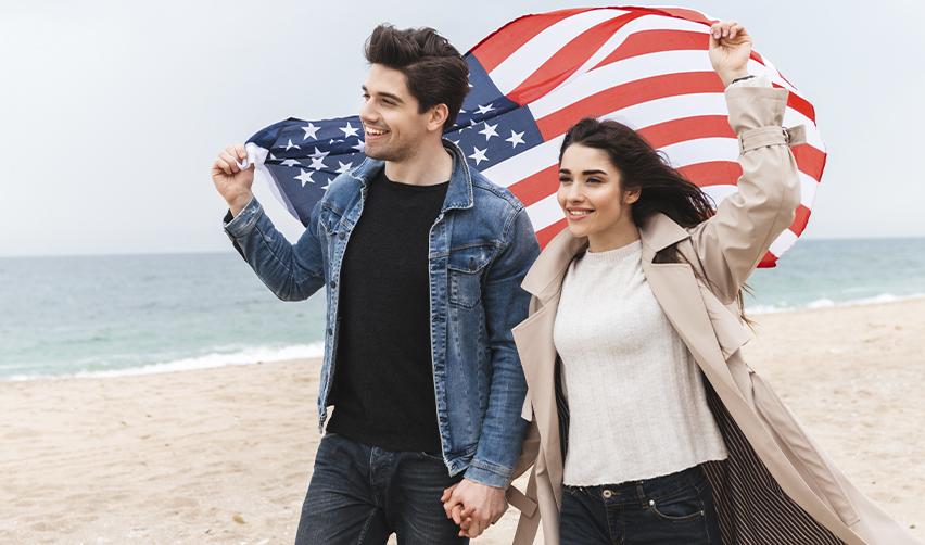 Smiling couple holding an American flag on a beach, representing successful immigration through the EB5 visa program.