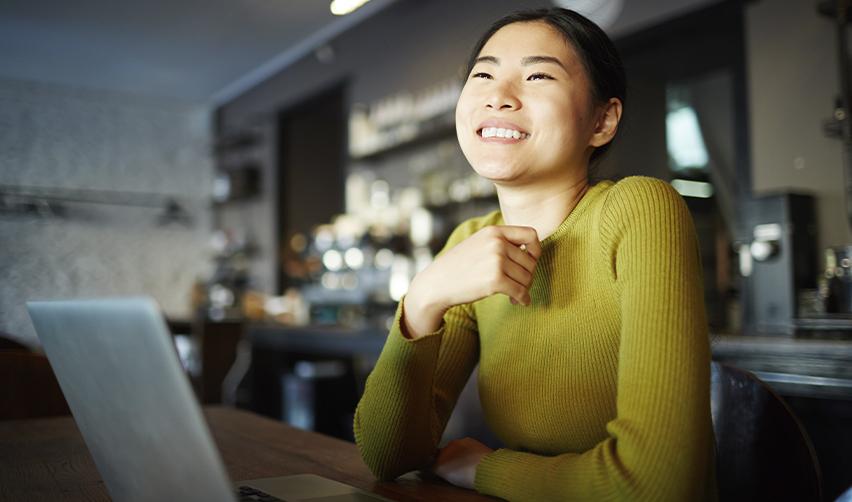 A smiling Asian woman at a laptop in a modern workspace, symbolizing optimism and EB5 visa success rate.