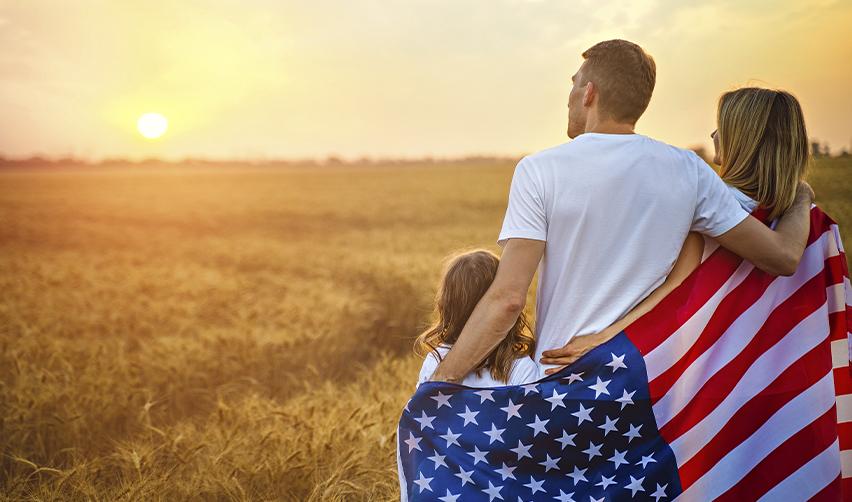 Family wrapped in the American flag, watching the sunset, illustrating the long-term security and opportunities provided by the EB5 program.