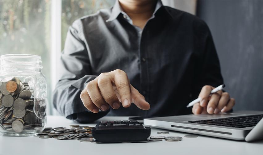 Person calculating finances with coins and a laptop, representing the financial planning involved in the EB5 investment process.