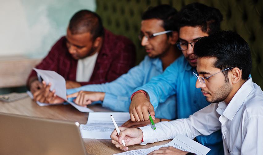 A group of Indian workers reviewing documents together, symbolizing the challenges of navigating U.S. immigration policies for H1B visa holders.