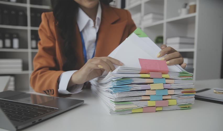 Close-up of a professional woman organizing a large stack of documents in an office. The complex paperwork process for H-1B visa applications and employment sponsorship.