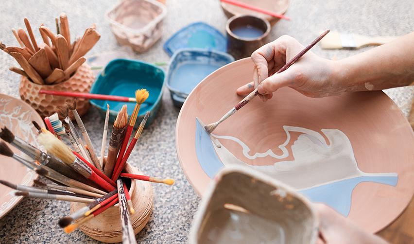 Close-up of hands painting a ceramic bowl during a pottery class at Club Cresswind's art center in Twin Lakes, emphasizing the creative opportunities available to residents.