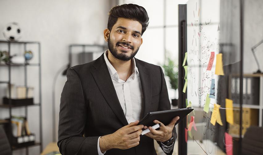 Indian entrepreneur in a business suit brainstorming ideas on a whiteboard, representing innovation and startup success in the U.S. through the EB5 visa program.