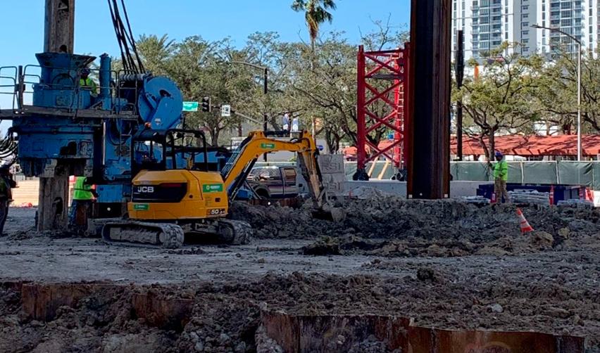 A construction site with a yellow excavator and a blue crane