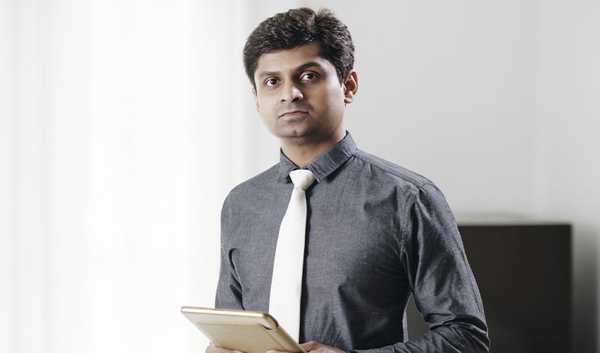 An Indian H1B holder holding a tablet stands in an office, illustrating the problems of skilled immigrants balancing career growth with evolving immigration policy regulations.