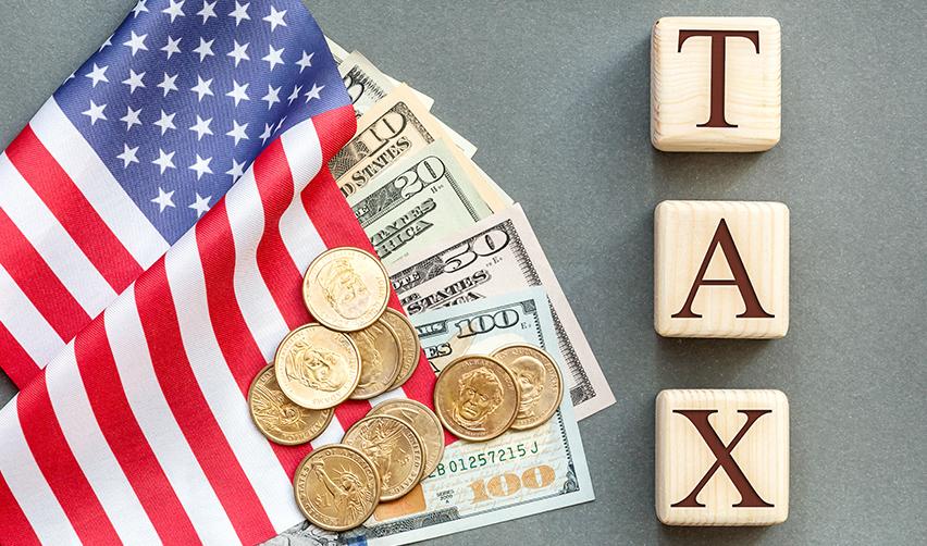 The word TAX next to an American flag and some U.S. dollars, symbolizing taxation on annual returns for EB5 investors.