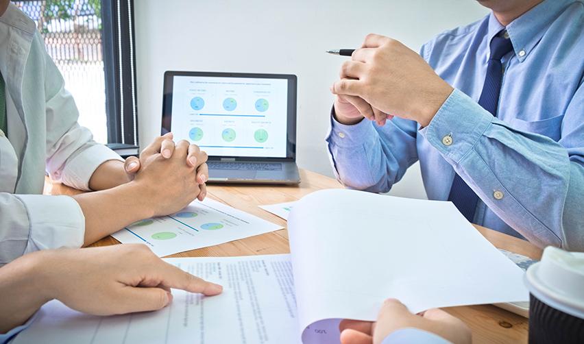 Close-up of business professionals discussing EB5 investment documents, with financial charts displayed on a laptop screen. A detailed review of project structure and financial security is essential for EB5 due diligence.