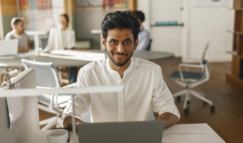 A young Indian professional working at his desk in a modern office, representing skilled H1B visa workers in the U.S. exploring permanent residency options like the EB5 program.