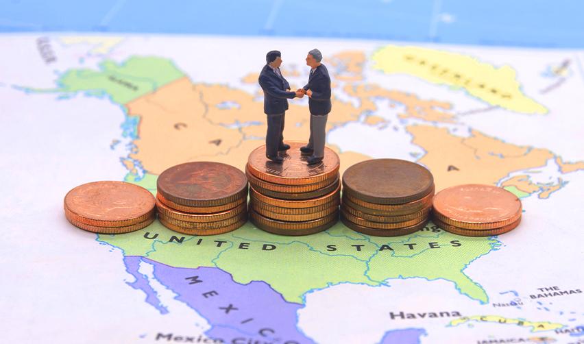 Miniature businesspeople shaking hands on stacked coins over a map of North America, symbolizing cross-border investment through the EB5 program.