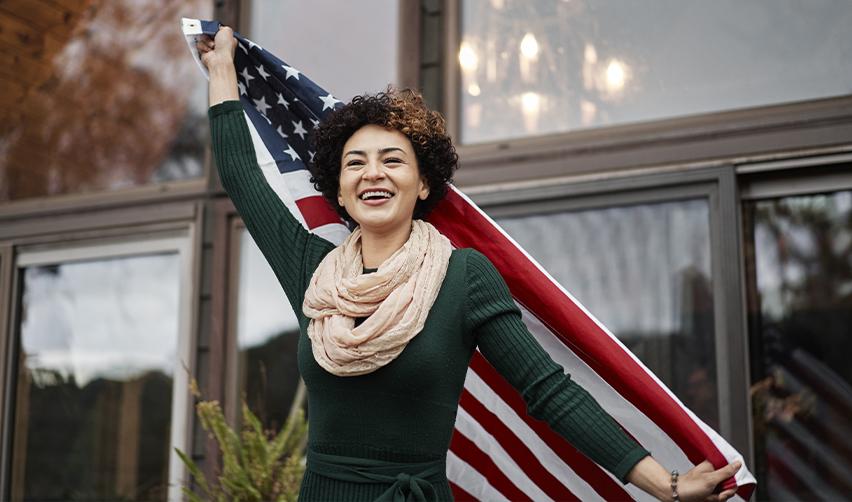 Smiling woman holding the American flag, symbolizing success in obtaining U.S. permanent residency through the EB5 program.