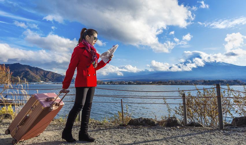 A woman holding a map and suitcase by a scenic lake, symbolizing the freedom of visa-free travel for EB5 Green Card holders.