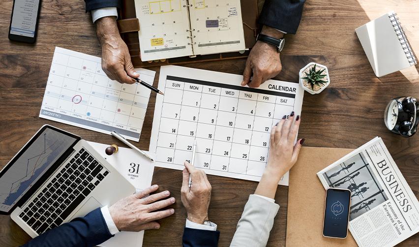 Business professionals planning project timelines with a calendar and laptop, symbolizing strategic planning for the EB5 process and fast-track investment approvals.