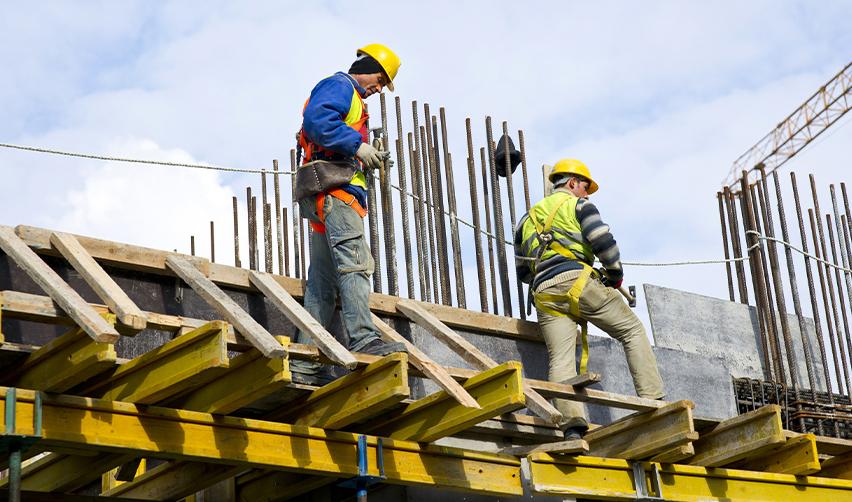 Two construction workers wearing safety gear working on a building framework, illustrating job creation and economic development in EB5 regional center projects.