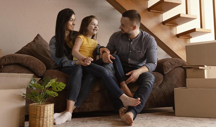 A family sitting on a couch surrounded by moving boxes, representing EB5 investors adjusting to their new life in the United States after immigration.