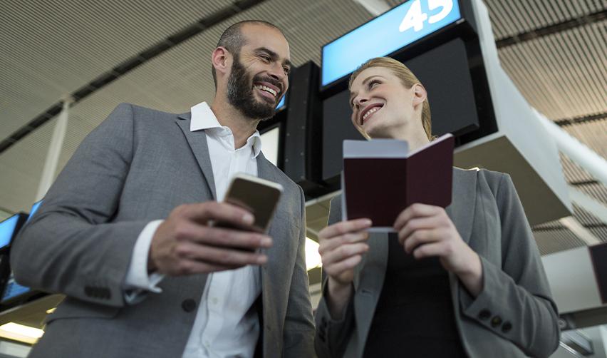 Two EB5 applicants in business attire smiling with passports at an airport, illustrating travel during the visa processing phase.