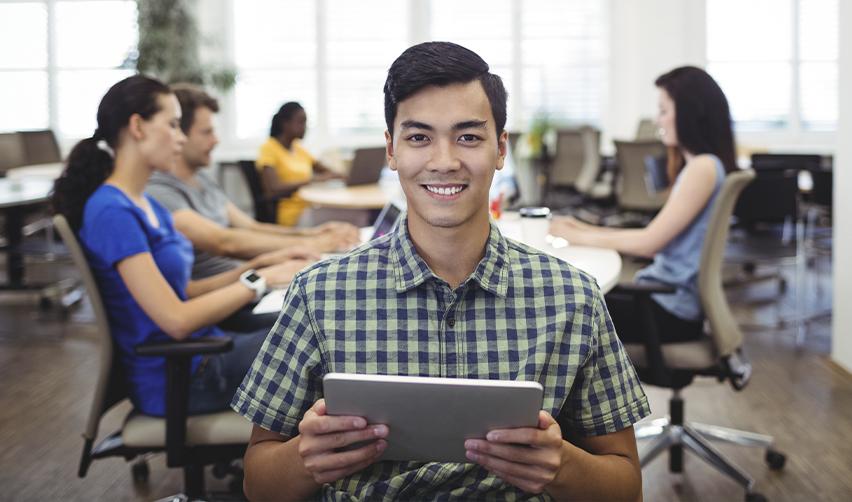 Smiling professional in a modern office holding a tablet, symbolizing H1B visa holders exploring EB5 visa options for faster Green Card access.