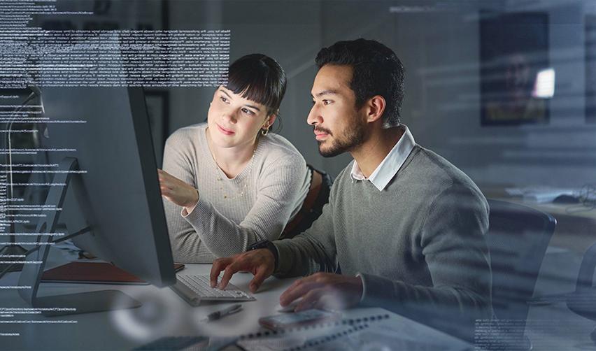 Two software developers collaborating at a modern workstation with code on screen, symbolizing tech professionals exploring EB5 visa opportunities for stability and Green Card access.