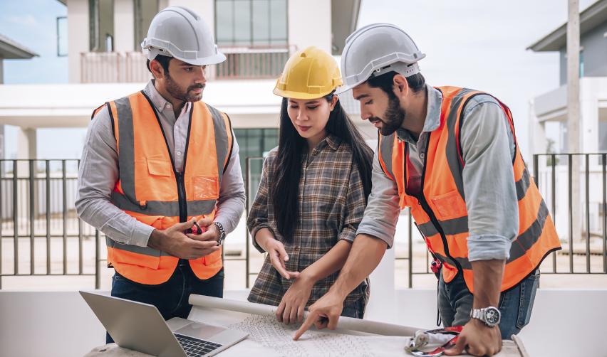 Three construction professionals in hard hats and safety vests reviewing building plans at a worksite, representing experienced EB5 project developers managing delivery timelines and investor capital.